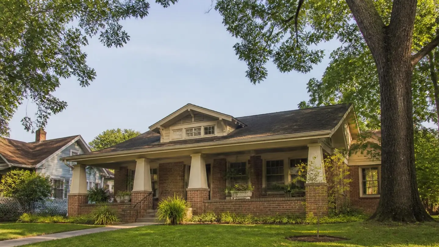 Craftsman-style brick bungalow with a deep front porch under mature oaks, typical of older Baton Rouge neighborhoods